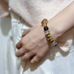 A person wearing a citrine bracelet on their wrist, showcasing its golden yellow crystals against a natural earthy setting to highlight the earth element.