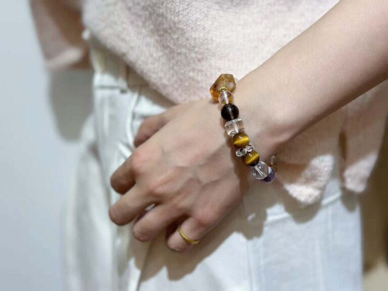 A person wearing a citrine bracelet on their wrist, showcasing its golden yellow crystals against a natural earthy setting to highlight the earth element.