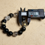 Golden sheen obsidian bracelet close-up with black base and golden flashes, captured on metallic water surface