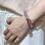 Super seven crystal bracelet with purple hue and metallic flashes, displayed on geometric background